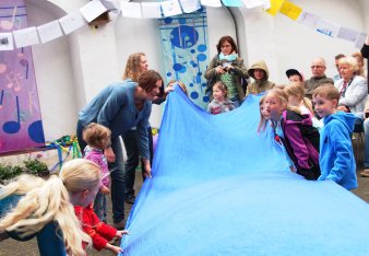 Kinder und Erwachsene haben im Hof der Musikschule aus einem großen blauen Tuch einen Fluss geformt.