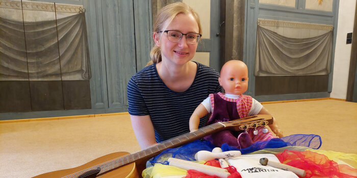 Lehrerin mit Baby-Puppe umgeben von Gitarre und elementaren Instrumentarium