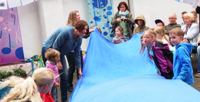Kinder und Erwachsene aus einem großen blauen Tuch einen Fluss geformt.