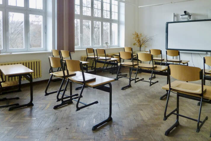 Das Foto zeigt einen Klassenraum der Schule vor der Sanierung mit Tischen und Stühlen sowie einer Tafel.
