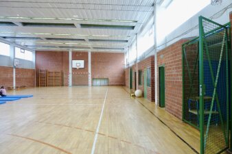 Das Foto zeigt die Sporthalle von innen vor der Sanierung mit Backstein-Wand und Holzboden.