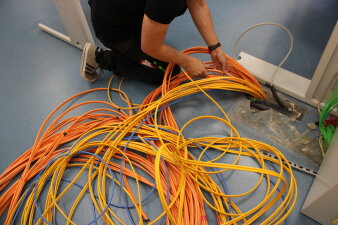 Das Foto zeigt einen Mitarbeiter, welcher an vielen verschiedenen Kabelsträngen arbeitet.
