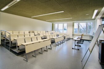 Das Foto zeigt den Hörsaal des GYM 10 mit weißen Bänken und Stühlen.