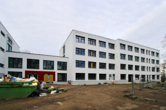 Das Foto zeigt die Schule mit weißer Fassade während der Sanierungsarbeiten von außen.