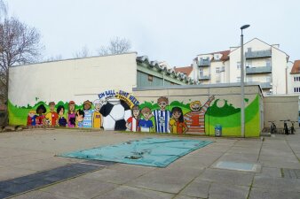 Das Foto zeigt die Sporthalle von außen vor der Sanierung mit bemalter Fassade.