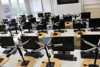 Das Foto zeigt ein möbliertes Klassenzimmer mit Fernseher und PC-Arbeitsplätzen.