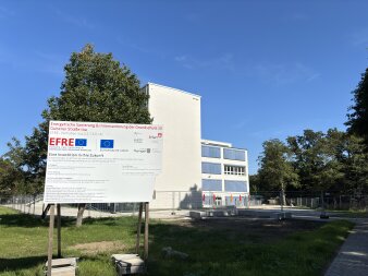 Das Foto zeigt das Schild zur Baumaßnahme und im Hintergrund das Schulgebäude der Grundschule Gispersleben.