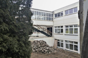 Das Foto zeigt das Schulgebäude mit weißer Fassade mit einer entfernten Außenwand.