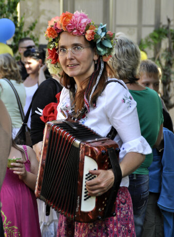 Eine Frau in Trachten und einem farbenprächtigen Blumenkranz im Haar spielt Akkordeon.