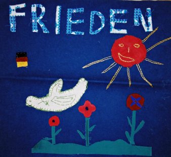 Textilbild mit Taube über Blüten auf blauem Grund. Darüber der Schriftzug "Frieden".