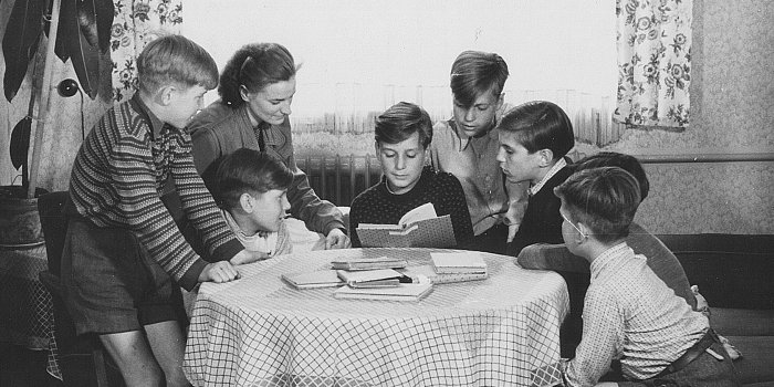 Kinder sitzen an einem Tisch, ein Junge liest.