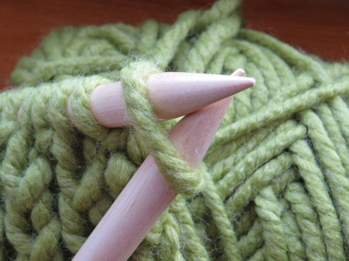 Wie beim Stricken, so muss man auch im richtigen Leben Ausdauer lernen, Schritt für Schritt, „Masche für Masche“ Strickzeug aus grüner Wolle.