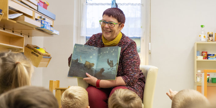 Frau zeigt einer Kindergruppe ein Kinderbuch.