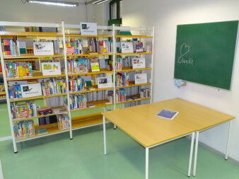 Ein Abteil mit Tafel, Tischen und einer Bücherregalreihe über Mathematik, Physik, Kunst und weiteren Schulfächern.