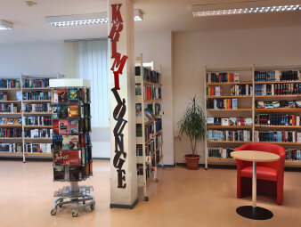 Ein Raum voller Bücherregale, einem Drehbuchständer, einer Sitzmöglichkeit und dem Schriftzug "Krimilounge".