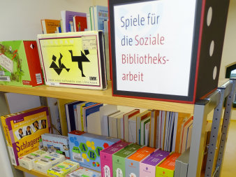 Ein mit Gesellschaftsspielen gefülltes Regal. Beschriftet mit "Spiele für die Soziale Bibliotheksarbeit".