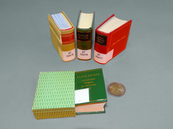 Abgebildet sind 4 Minibücher in verschiedenen Farben. Eine Zwei-Euro-Münze liegt als Größenvergleich bei.