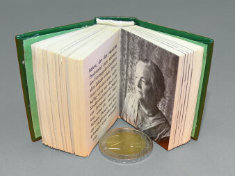 Ein aufgeklapptes Minibuch mit einer Abbildung von Clara Zetkin. Darunter eine Zwei-Euro-Münze als Größenvergleich.