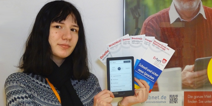 Eine junge Dame präsentiert die Onlinedienste der Bibliothek Erfurt anhand von aufgefächerten Flyern.