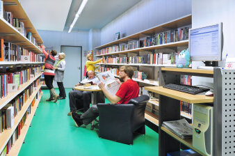 Innenansicht der Bibliothek Südpark. Leute stöbern in den Regalen und lesen Zeitung. 