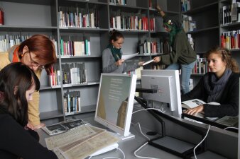 junge Bibliotheksnutzerinnen arbeiten an Computern und holen Bücher aus dem Regal