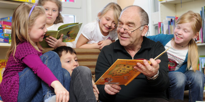 Ein Mann liest Kindern aus einem Buch vor. 