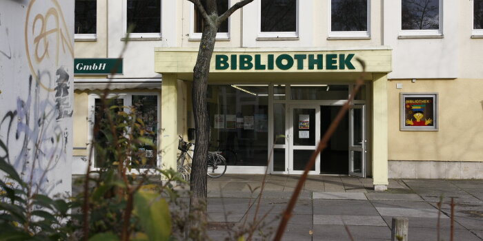 ein Stapel Bücher liegt im Fenster hinter dem ein Neubaublock zu sehen ist