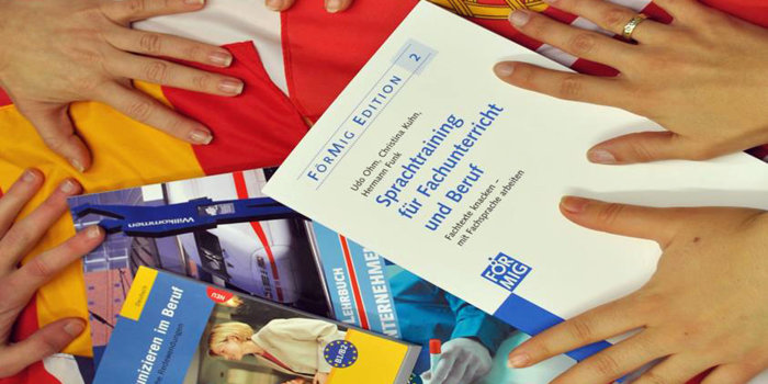 Foto: Berufsbezogene Deutschförderung © Volkshochschule Erfurt Vier Hände greifen sich Unterrichtsbücher.