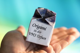 Foto: Kleine Geschenkverpackungen selbst gemacht © Stadtverwaltung Erfurt / Grit Kästner Auf einer Hand liegt eine im Origami gefertigte Geschenkverpackung mit der Aufschrift: "Origami in der VHS Erfurt".