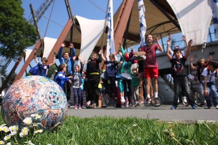 Fußballbegeisterte Kinder im Hintergrund vor dem Steigerwaldstadion in Erfurt. Ein Fußball im Vordergrund.