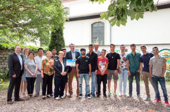 Minister Lauinger überreicht einen symbolischen Scheck an eine Gruppe von Teilnehmenden des Pilotprojektes "Landesprogramm Start Deutsch". 