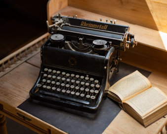 Historische Schreibmaschine auf Holztisch, daneben ein altes Buch.