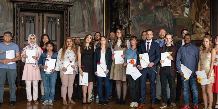 Foto: Die Absolventinnen und Absolventen der Sprachkurse, des Realschulabschlusses und des Abitur bekamen im Rathausfestsaal ihre Zertifikate und Zeugnisse überreicht © Stadtverwaltung Erfurt Viele Menschen in einem Festsaal halten ihr Zeugnis in den Händen.