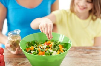 Kind greift in eine grüne Schüssel mit Möhren und Salat.