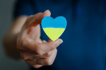 Ein Holzherz in der Hand, welches in den ukrainischen Farben hellblau und gelb bemalt ist.