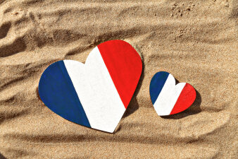 Zwei Herzen aus Holz liegen auf Sand und sind mit den französischen Nationalfarben bemalt.
