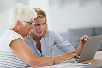 Eine ältere und eine jüngere Frau sitzen vor einem Computer.