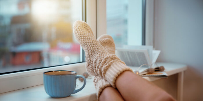 Bildungsfreistellungskurse an der Volkshochschule Erfurt Füße mit Wollsocken im Fenster liegend, daneben eine Tasse und ein Buch.