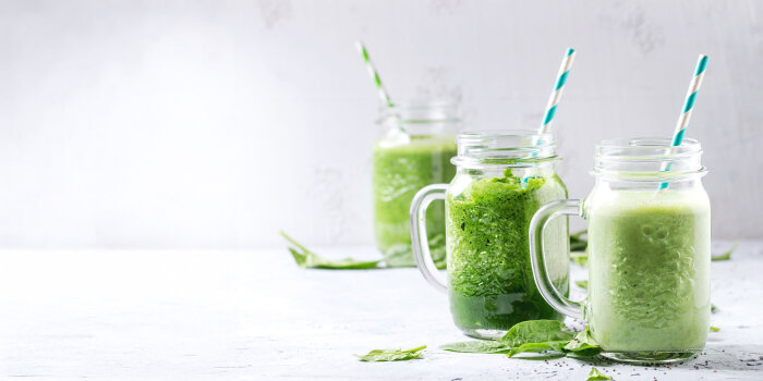 Smoothiekräuter im Winer Auf einem weißen Tisch stehen drei Gläser mit Trinkröhrchen und grünem Smoothiekräutergetränk.