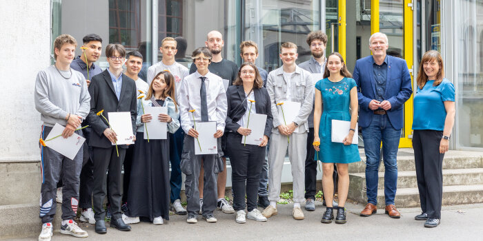 15 Personen, von denen einige eine Urkunde und eine Blume in der Hand halten