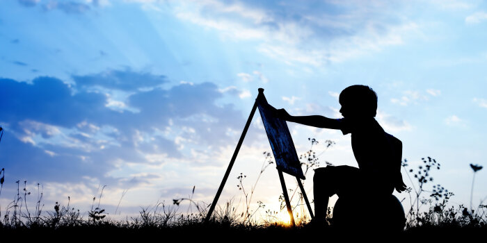 Vor blauen Himmel sitzt als Silhoutte auf einem Feld mit Blumen ein kleiner Junge vor einer Staffelei und malt.