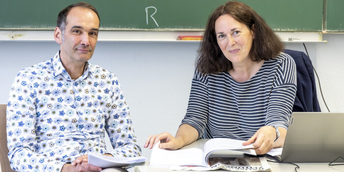 ein Mann und eine Frau sitzen an einem Tisch vor einer Wandtafel