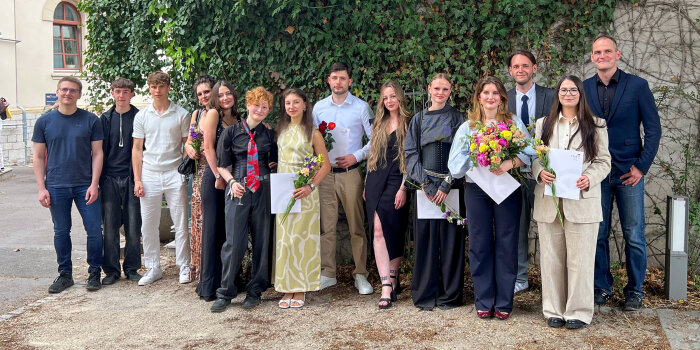 eine Gruppe von 14 vorwiegend jungen Menschen, einige halten Urkunden und Blumen in der Hand