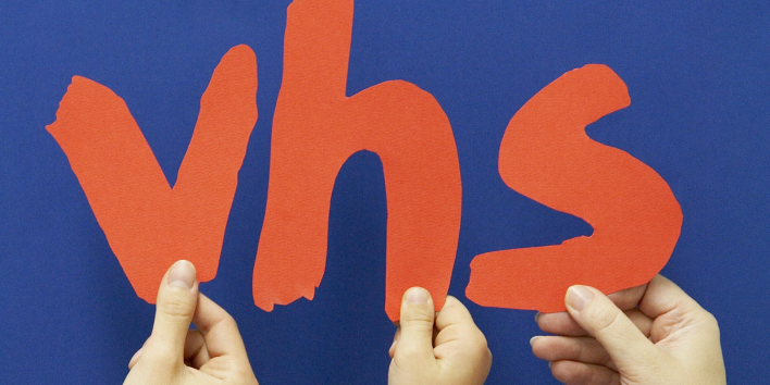 Bild: Logo der Volkshochschule © Landeshauptstadt Erfurt, Stadtverwaltung Vor einem dunkelblauen Hintergrund halten drei Hände jeweils einen Buchstaben des Volkshochschullogos in die Höhe.