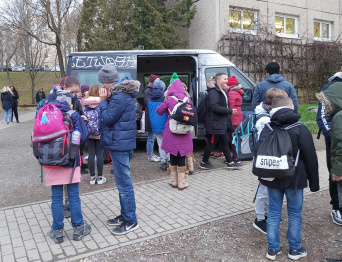 Streetworker Süd Kinder und Jugendliche auf einem Schulhof, dahinter ein Fahrzeug.