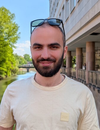Ein bärtiger Mann mit Sonnenbrille auf dem Kopf steht auf einer Brücke und lächelt in die Kamera.