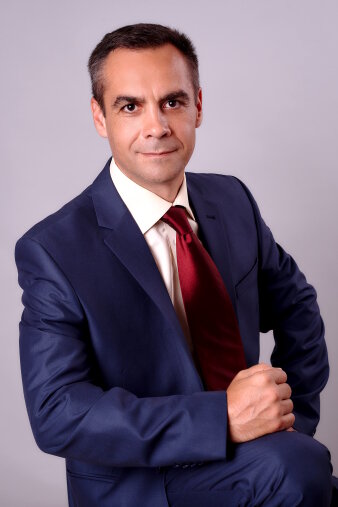 Ein Mann mit blauem Anzug und roter Krawatte lächelt in die Kamera.