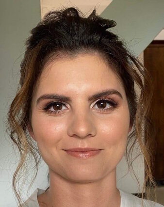 Eine Frau mit braunen Augen trägt eine Hochsteck-Frisur und lächelt in die Kamera.