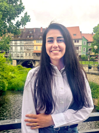Eine Frau, mit langen schwarzen Haaren, steht auf einer Brücke, im Hintergrund ist die Krämerbrücke zu sehen.