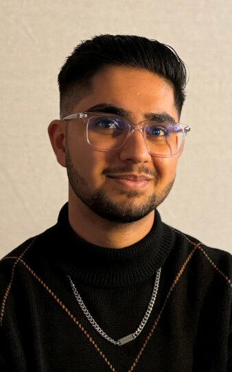 Ein Mann im schwarzen Pullover und mit transparenter Brille lächelt in die Kamera.